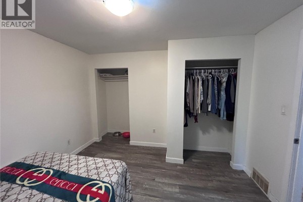 Bedroom with white walls, dark patterned bedding, and two large open closets. - 113 109th Street W, Saskatoon