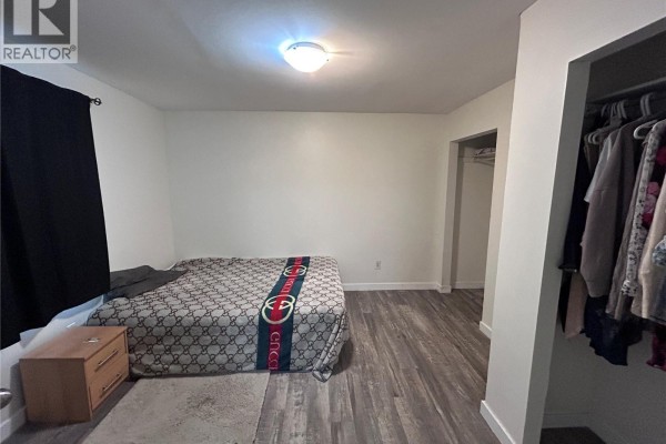 Bedroom with bed, nightstand, and two open closets filled with clothes. - 113 109th Street W, Saskatoon