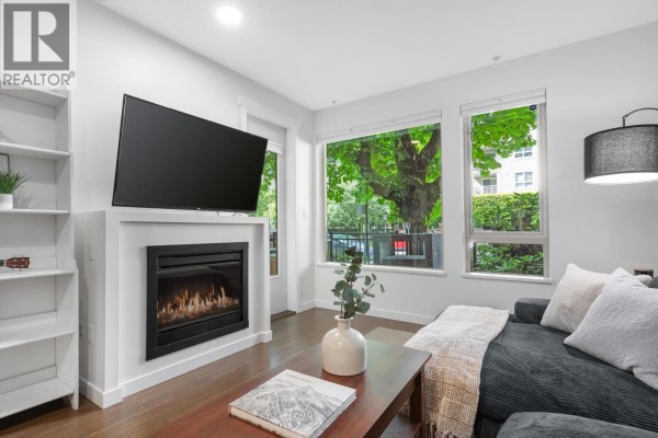 Living room fireplace with mounted television and large windows overlooking greenery. - 113 119 W 22nd Street, North Vancouver