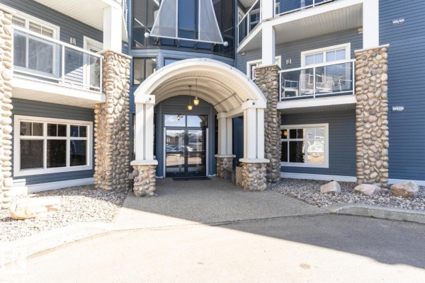 Exterior view of a multi-story apartment building with balconies and grey siding. - #113 16035 132 St Nw, Edmonton
