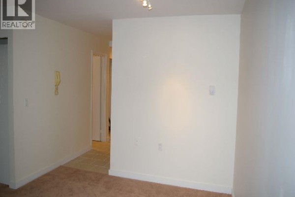 A beige carpeted room has off-white walls, a beige telephone, and a tiled hallway entrance. - 113 707 8 Street, New Westminster
