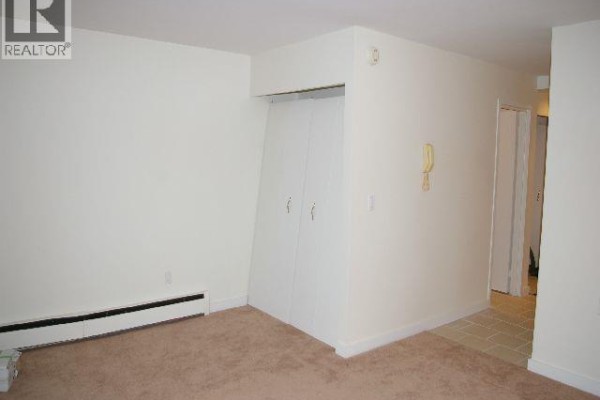 A beige carpeted room features off-white walls, bi-fold closet doors, and a baseboard heater. - 113 707 8 Street, New Westminster