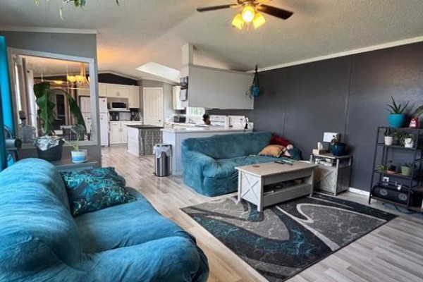 Living room with teal sofas, a coffee table, and an open view to the kitchen. - 113 Clark Crescent, Rural Grande Prairie No  1, County Of