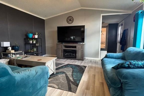 Living room with teal sofas, a television, and a view into a hallway. - 113 Clark Crescent, Rural Grande Prairie No  1, County Of