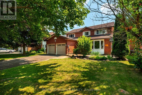 Side exterior view of a brick house with a double garage, lawn, and large green trees. - 113 Meadow Drive, Orangeville