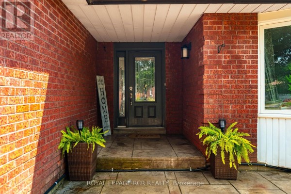 Covered front entryway with brick facade, stone tile, and a dark wood door with glass panels. - 113 Meadow Drive, Orangeville