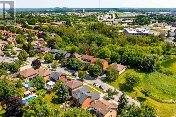 Aerial view of a suburban neighborhood with mature trees, houses, and a wooded area in the background. - 113 Meadow Drive, Orangeville