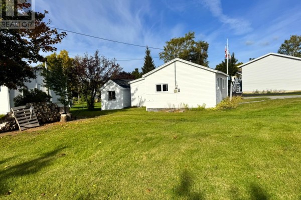 Rear view of the white vinyl-sided house and a small shed on a large green lawn with trees. - 113 Midland Row, Pasadena