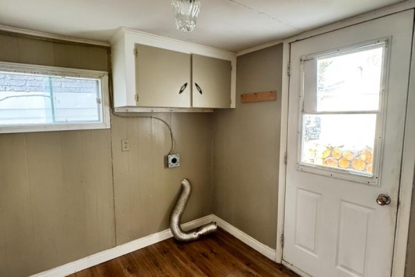 Corner of a room with wood floors, beige walls, a window, overhead cabinets, and a metal dryer vent pipe. - 113 Midland Row, Pasadena
