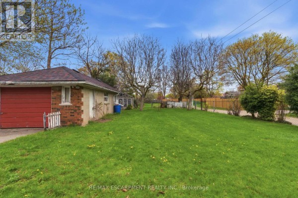 Side view of a brick garage with a red door and a large grassy backyard. - 113 North Park Street, Brantford