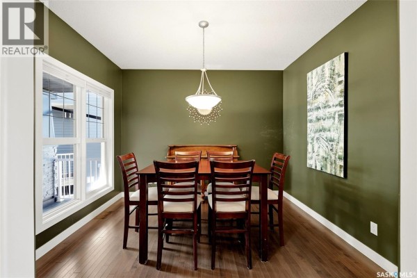Dining room with dark green walls, hardwood floors, and a dark wood table with six chairs. - 113 Poplar Bluff Crescent, Regina