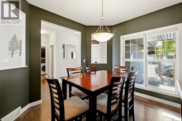 Dining room with dark green walls, hardwood floors, a dining table, and a view of the backyard. - 113 Poplar Bluff Crescent, Regina