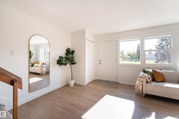 Interior entryway with light wood flooring, white walls, a large arched mirror, and a sofa. - 113 Village On The Green Gr Nw, Edmonton