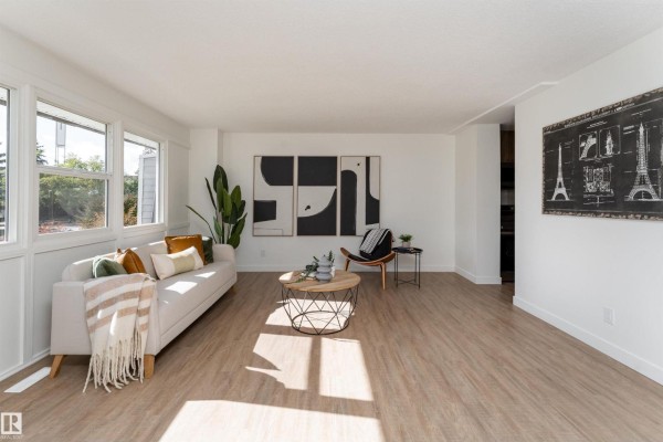 Spacious living room with light wood floors, white walls, sofa, coffee table, and wall art. - 113 Village On The Green Gr Nw, Edmonton