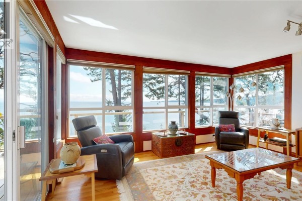 Living room with leather recliners, coffee table, and large windows with ocean view. - 1130 Berry Point Rd, Gabriola Island