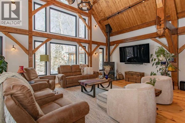 Living room with vaulted timber ceiling, fireplace, large windows, and upholstered seating arrangements. - 1130 Breakers Way, Sunbreaker Cove