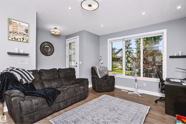 Living room with grey walls, dark grey reclining sofa, armchair, and large window. - 11305 79 Av Nw, Edmonton