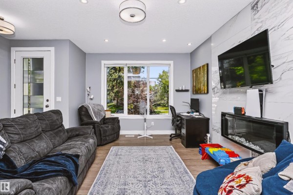 Living room with grey walls, fireplace, television, and window overlooking the backyard. - 11305 79 Av Nw, Edmonton