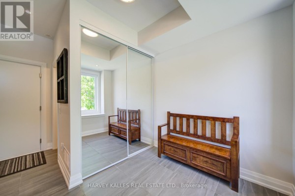Interior space with a wooden bench, large window, and a mirrored closet door reflecting the bench. - 1130a Islington Avenue, Toronto