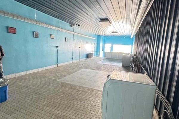 Long commercial interior space with blue walls, tiled floor, and multiple washing machines. - 1132 Fifth Street, Estevan