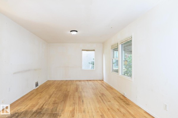 Empty living room with light-colored walls, hardwood floors, and two windows. - 11321 89 St Nw, Edmonton