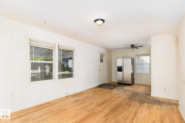 Room with hardwood floors, white walls, two windows, and a stainless steel refrigerator. - 11321 89 St Nw, Edmonton