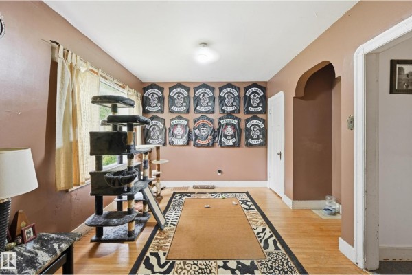 Living room with wood floors, taupe walls, a large cat tree, and jackets displayed on the wall. - 11325 101 St Nw, Edmonton