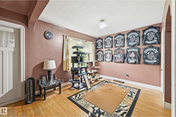 Living room with wood floors, taupe walls, a cat tree, a large rug, and jackets displayed on the wall. - 11325 101 St Nw, Edmonton