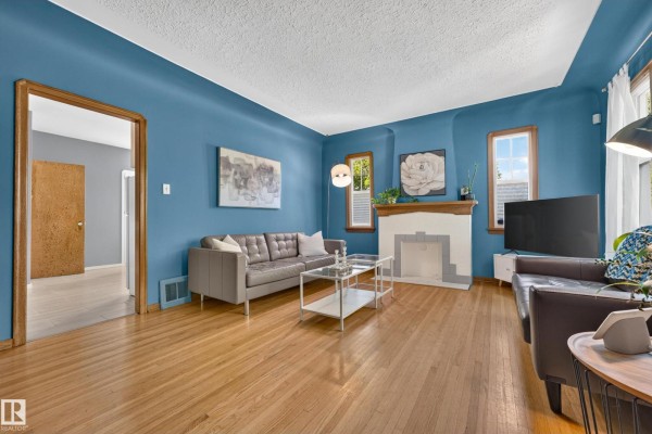 Living room with blue walls, a grey sofa, a fireplace, and hardwood floors. - 11346 69 St Nw, Edmonton