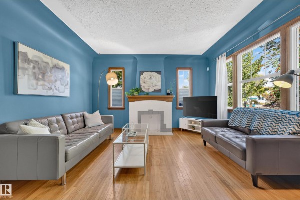 Living room with two grey sofas, a fireplace, hardwood floors, and large windows. - 11346 69 St Nw, Edmonton