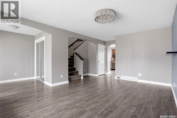 Living room with wood-look flooring, staircase, and doorway to kitchen. - 1137 Jurasin Street N, Regina