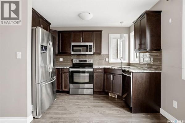 Kitchen with dark wood cabinets, stainless steel appliances, and granite countertops. - 1137 Jurasin Street N, Regina