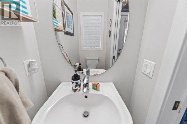 A small powder room with a white sink, chrome faucet, oval mirror reflecting the toilet, and blinds. - 114, 300 Marina Drive, Chestermere