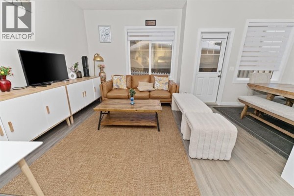 Living room with a tan sofa, wooden coffee table, long console, and a jute rug on a wood-look floor. - 114, 300 Marina Drive, Chestermere