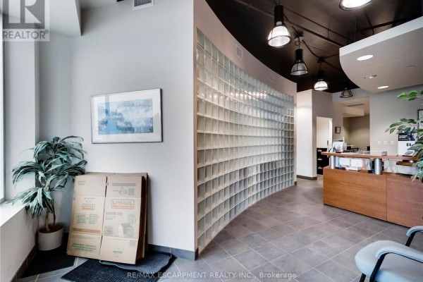 Interior reception area with gray tile floor, curved glass block wall, and stacked moving boxes near a window. - 114 - 1100 South Service Road, Hamilton