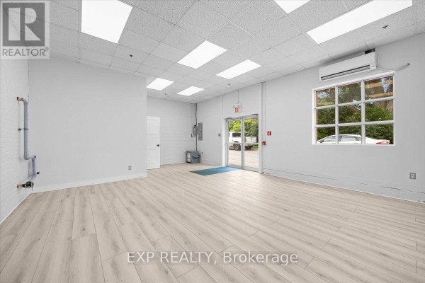 Empty commercial interior with white walls, light wood laminate flooring, drop ceiling with fluorescent lights, and views of trees through the windows. - 114 - 40 Sunset Boulevard, Perth