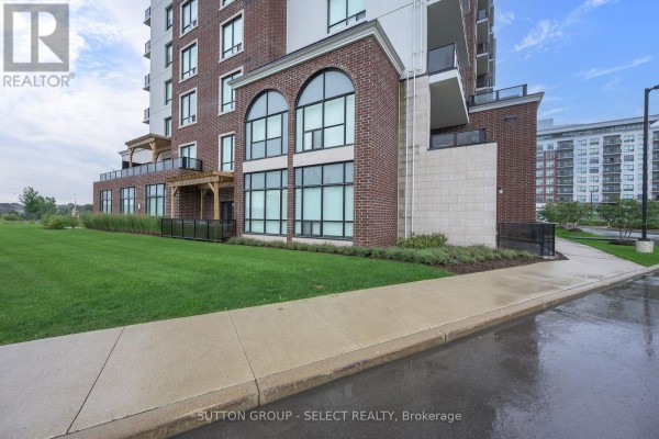 View of apartment building exterior with large arched windows, brick facade, and manicured lawn. - 114 - 480 Callaway Road, London North