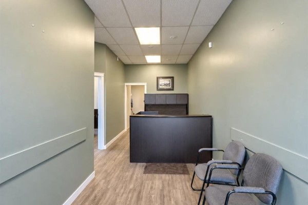Office reception area with a dark wood desk, chairs, and a doorway leading down a hallway. - 114 5th Avenue N, Swan River