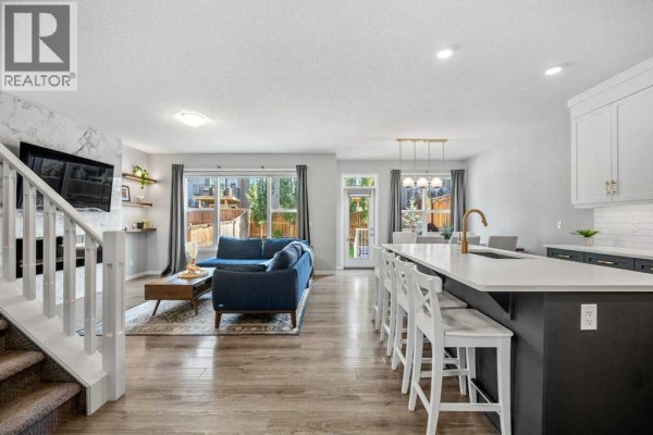 Open concept living and kitchen area with blue sectional, fireplace, and island. - 114 Crestbrook Way Sw, Calgary