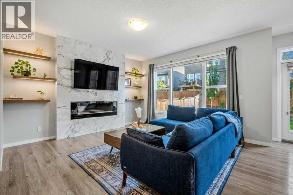 Living room with a large marble fireplace, television, blue sectional sofa, and wood floors. - 114 Crestbrook Way Sw, Calgary