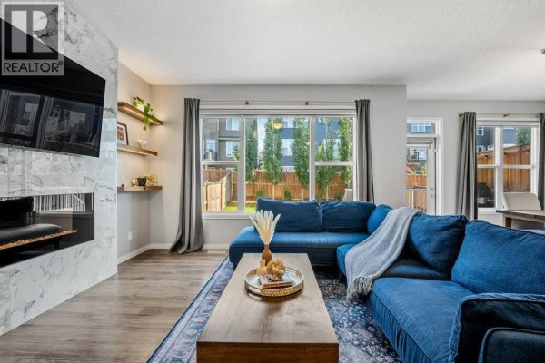 Living room with a fireplace, large windows, and a blue sofa with a throw blanket. - 114 Crestbrook Way Sw, Calgary