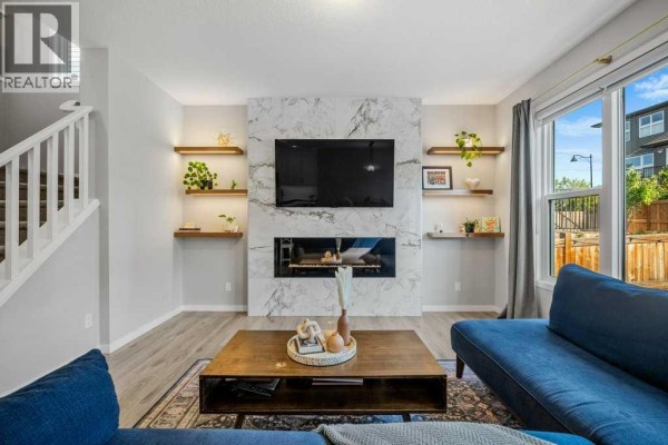 Living room featuring a modern fireplace, wall-mounted television, and built-in shelving. - 114 Crestbrook Way Sw, Calgary