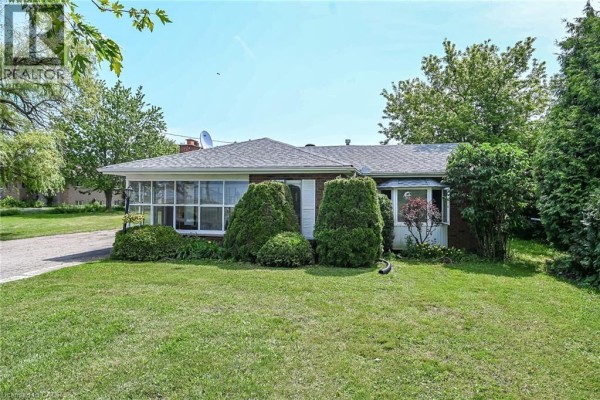Front facade of the bungalow with manicured bushes and green lawn. - 114 Second Road E, Stoney Creek