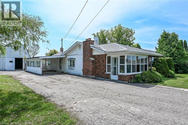 Side view of the bungalow, highlighting the brick chimney and sunroom addition. - 114 Second Road E, Stoney Creek