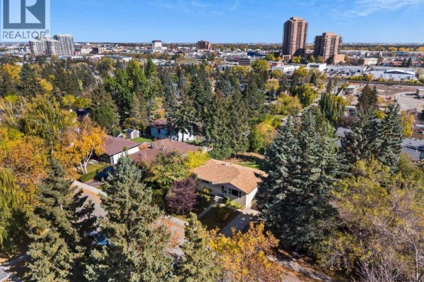 Aerial view of the property surrounded by mature trees and city skyline. - 114 Havenhurst Crescent Sw, Calgary
