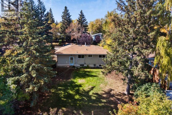 Rear exterior of the house with a grassy backyard and trees. - 114 Havenhurst Crescent Sw, Calgary