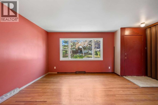Empty living room with pink walls, hardwood floors, and a large window. - 114 Havenhurst Crescent Sw, Calgary