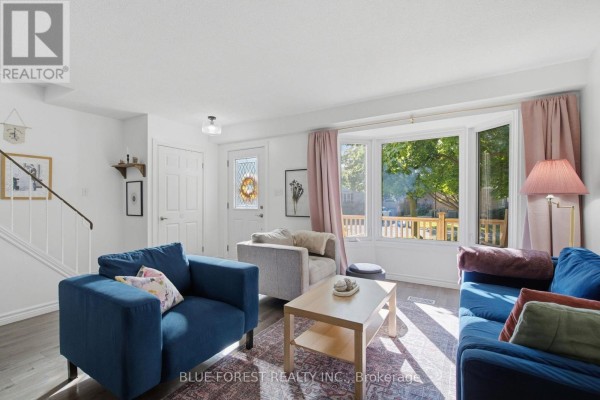 Living room with a bay window, blue and grey sofas, and a wooden coffee table. - 114 Hearthside Place, London East