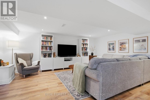 Finished basement living area with a large grey sectional, TV, and built-in bookshelves. - 114 Hearthside Place, London East