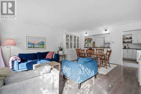 Living room and dining area with blue sofa, wooden table, and white kitchen cabinets. - 114 Hearthside Place, London East